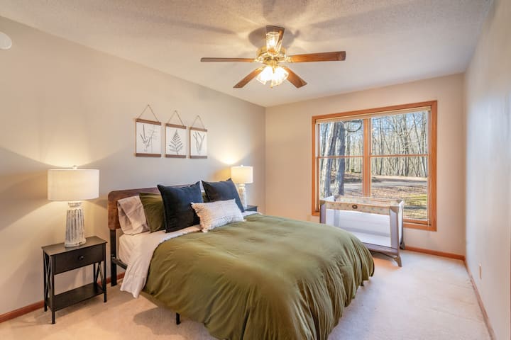 Spacious guest room with a cozy queen bed, tranquil forest views, and inviting décor details — plus a pack-n-play for added convenience.