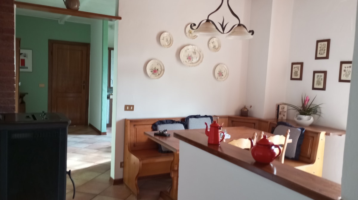 A dining area is featured with a wooden table bordered by fitted seating. Decorative plates adorn the wall above, while a chess set is positioned on the table. A teapot and a smaller ceramic teapot are placed on the surface, adding a touch of charm.