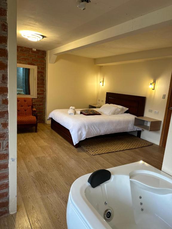 A spacious bedroom is presented with a large bed and essential bedside tables. A cozy chair in the corner complements the room’s warm tones. A subtle jacuzzi is visible in the foreground, enhancing the luxurious ambiance of the space.