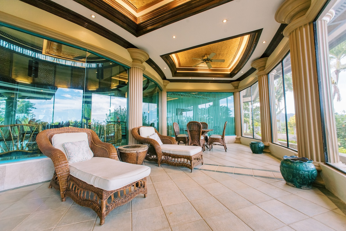 An inviting screened porch features comfortable lounge chairs and a wicker seating area. Floor-to-ceiling glass offers panoramic views of the surrounding landscape. Decorative elements, including planters, enhance the serene atmosphere, allowing for a peaceful retreat indoors.