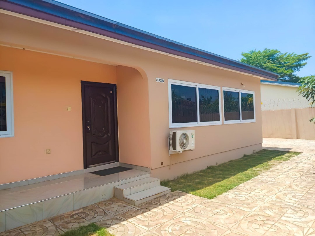 The exterior of the home is displayed, showcasing a light peach facade with large windows that offer abundant natural light. A neatly arranged front pathway leads to the entrance, and well-maintained grass lines the edges of the property under a clear blue sky.