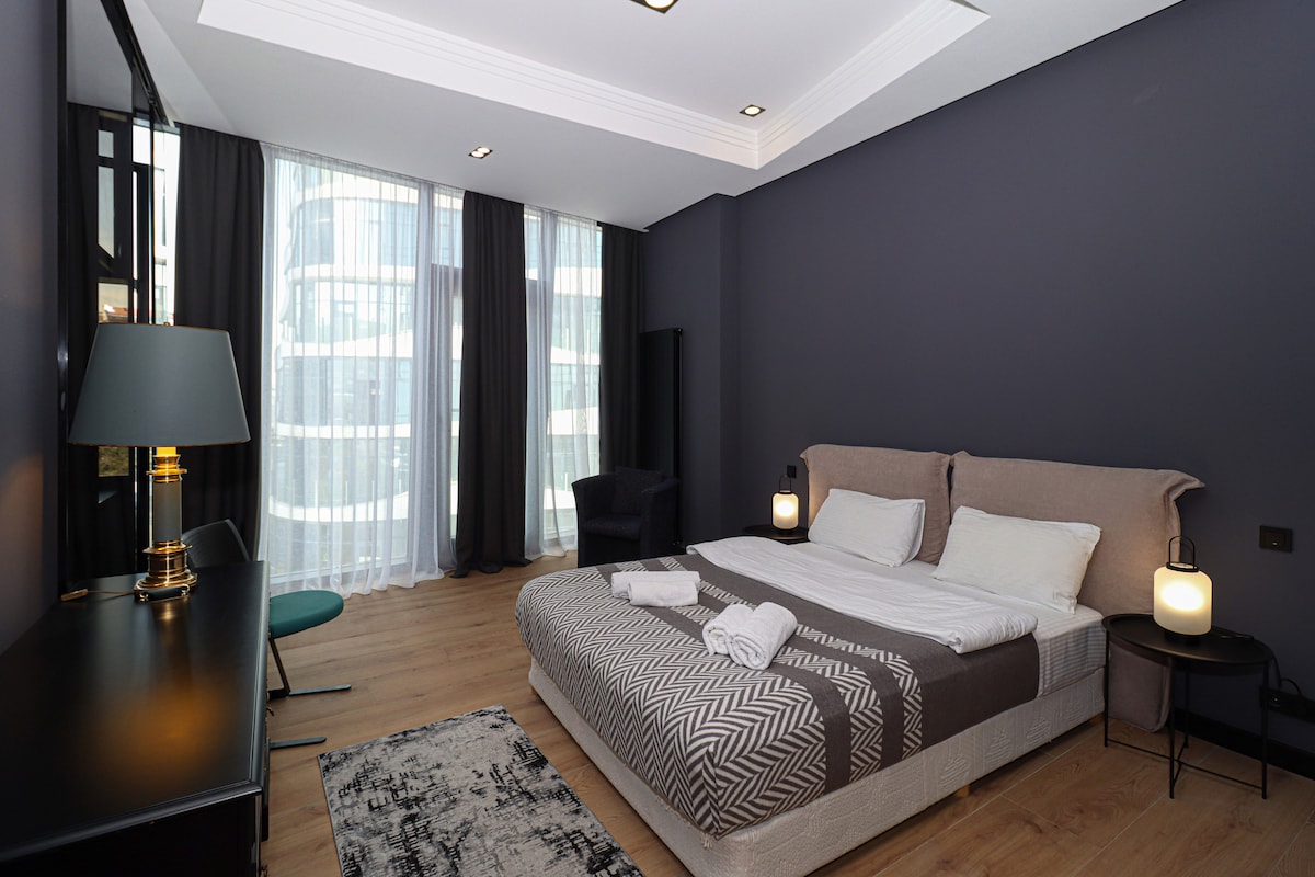 El dormitorio incluye una cama tamaño king, una mesita de noche negra, lámparas de noche y varias opciones de asientos.