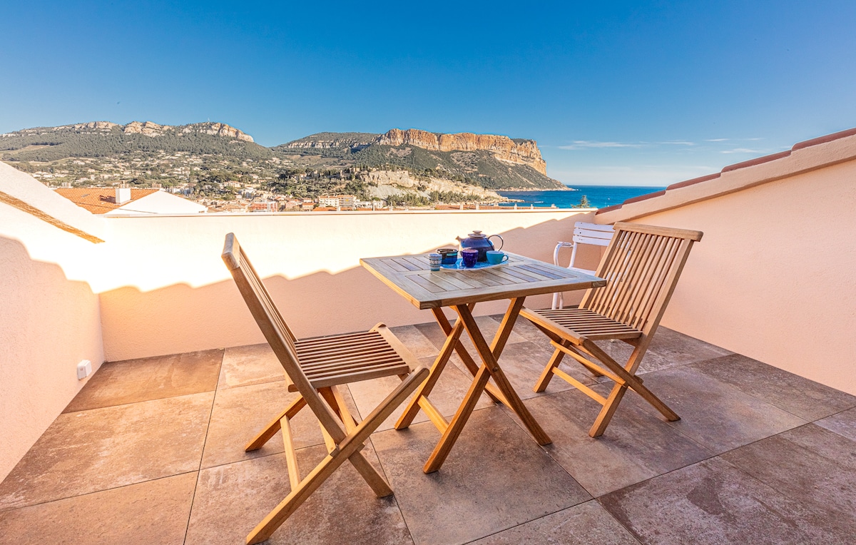 A private terrace is shown with a wooden table and two folding chairs, set against a scenic backdrop of the sea and Cap Canaille. The area is sunlit, and the horizon showcases a clear blue sky, enhancing the outdoor experience.