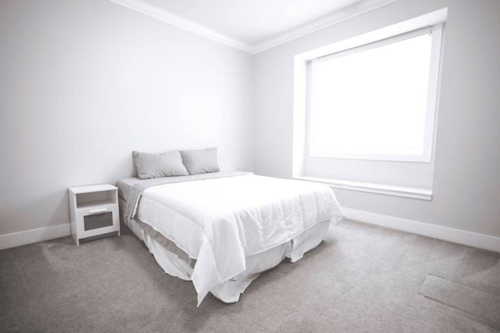 Spavaća soba ima udoban bračni krevet, noćni ormarić i velike prozore koji pružaju dovoljno prirodnog svjetla.