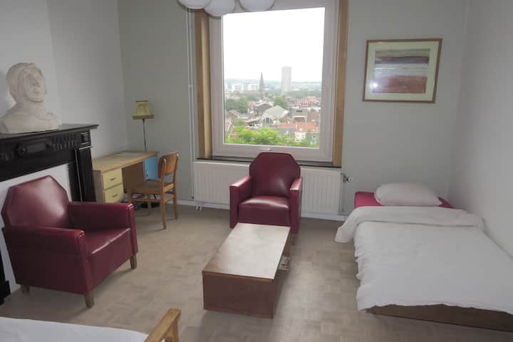 Overview of your large living room with city views. Office area and small living room, extra bed convertible into a bench, double bed at the front of the photo. The bathroom is attached and locked.