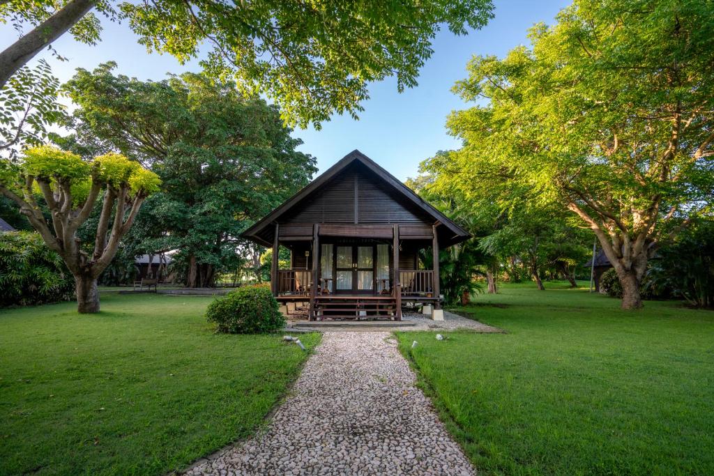 A charming cottage is framed by lush greenery and well-maintained lawns. A stone pathway leads to a welcoming porch with ample seating. Large windows flank the front, allowing natural light to brighten the interior.