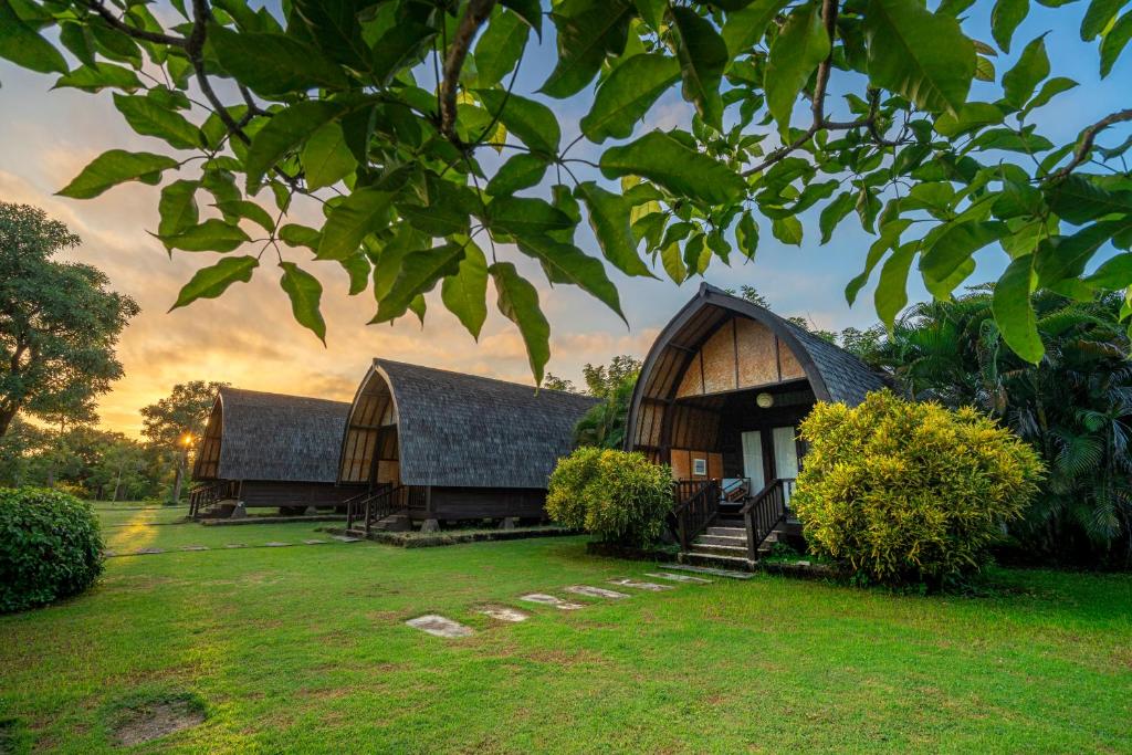 Several charming bungalows with sloped roofs are surrounded by lush greenery and a well-maintained lawn. The setting features a serene atmosphere with a vibrant sunset sky in the background, providing a peaceful retreat amidst nature.