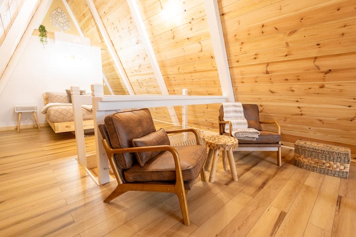 Upstairs bedroom with Queen size bed, mini split AC and heating unit, on suite half bath, reading nook with two chairs, a coffee table, and chest with extra blankets