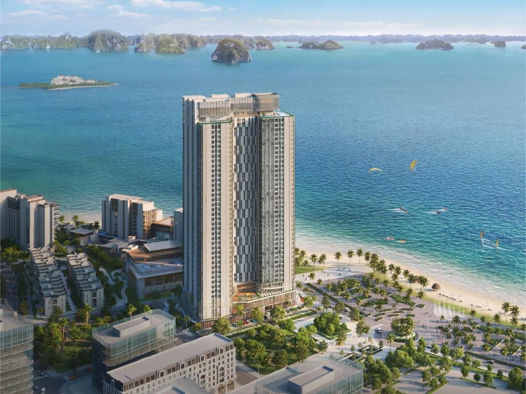 A modern high-rise building is positioned along a sandy beach, showcasing a blend of glass and concrete finishes. Surrounding palm trees and landscaped areas complement the coastal setting, with distant islands visible in the turquoise waters of the ocean.