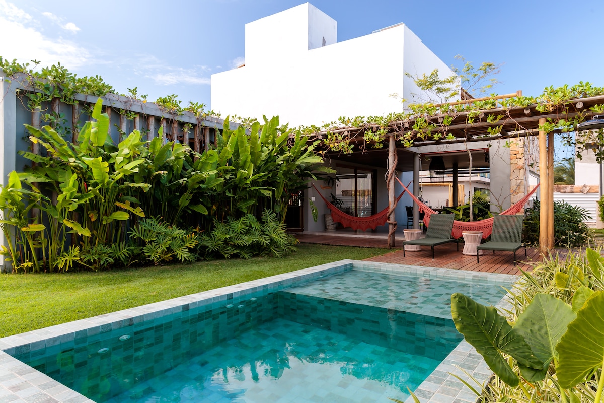 A tranquil outdoor area is presented with a private pool surrounded by lush greenery. Comfortable lounge chairs and hammocks are positioned under a trellis, inviting relaxation. The open layout offers seamless access to the nearby living spaces, enhancing the connection with nature.