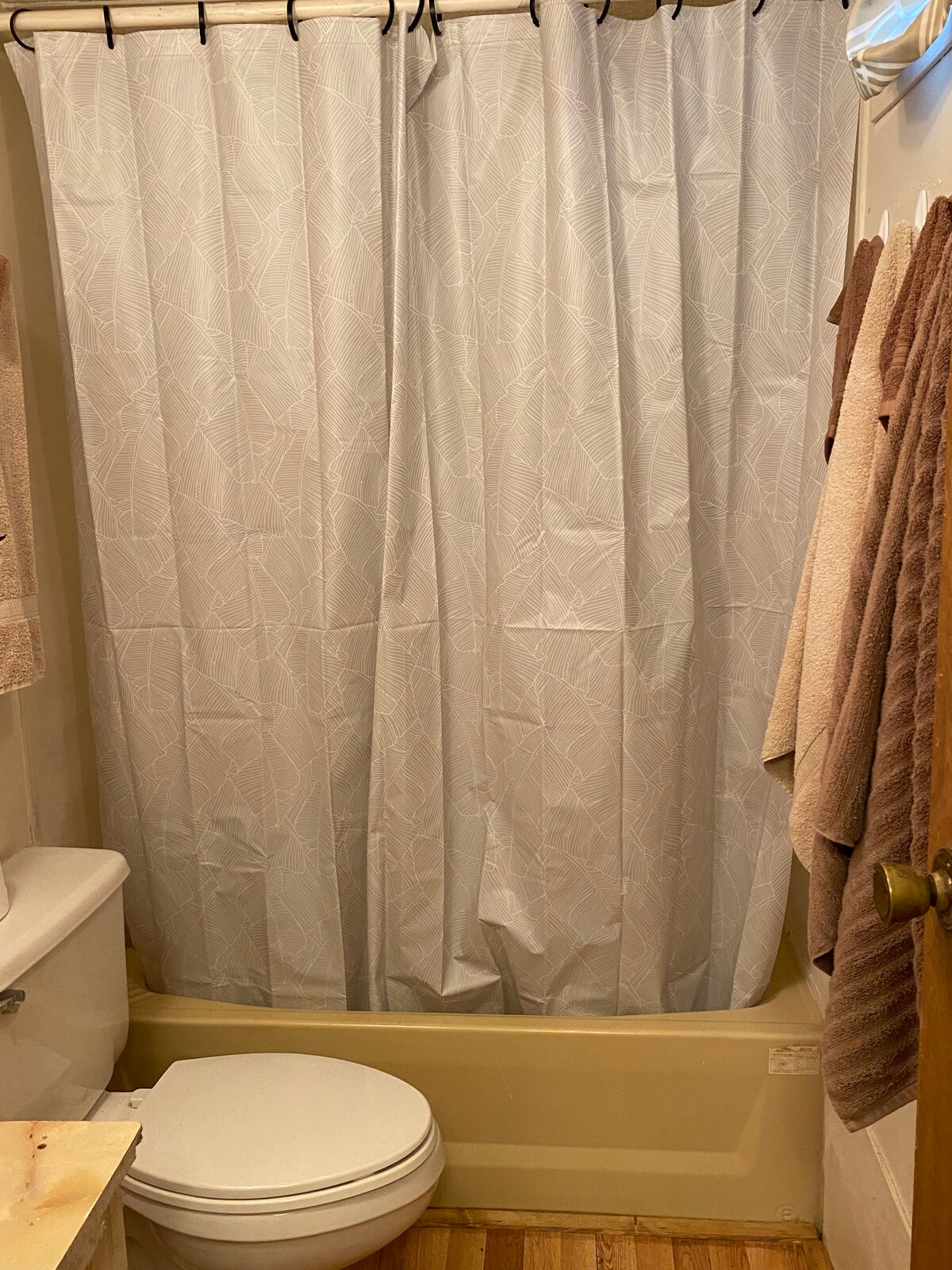 The bathroom features a neutral-colored shower curtain, providing privacy for the shower area. A compact toilet is positioned beside the bathtub, while neatly arranged towels hang on a rack nearby, contributing to the room's functional layout.