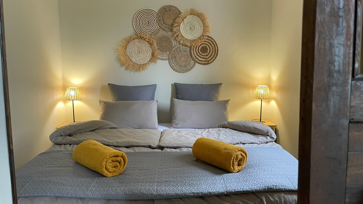 חדר השינה הראשי עם מיטת קינג סייז, 2 שידות לילה עם מנורות, שרפרף, מראה קטנה וארון קיר. יש לכם חלון לגינה עם תריסי במבוק ווילונות.