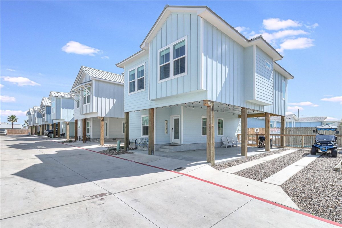 A row of modern beach houses features light blue exteriors and large windows allowing natural light indoors. Each house is elevated with a spacious area underneath, where seating is arranged. A golf cart is parked nearby, providing convenient access for guests.