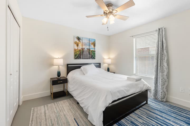 Elegante dormitorio de Navarre Beach con cama tamaño queen, TV de tamaño completo, ventilador de techo y cortinas que oscurecen la habitación. Meticulosamente limpio y cuidadosamente diseñado para la comodidad y la relajación: tu refugio costero perfecto para una noche de sueño reparador después de la playa