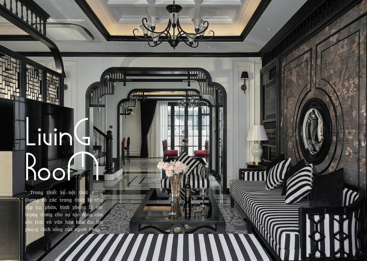 A stylish living room is presented with a striking monochrome color scheme. Vertical and horizontal striped patterns adorn the sofas, while elegant lighting fixtures hang from the ceiling. Decorative metal accents are featured on the walls, creating a sophisticated atmosphere with a modern aesthetic.