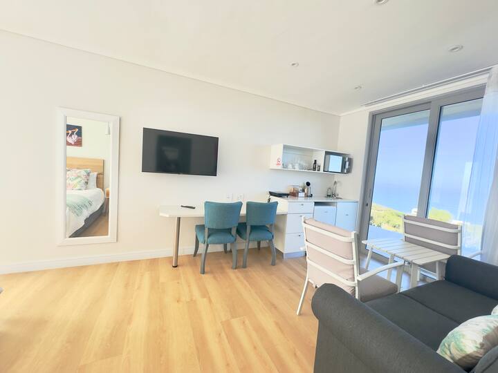 Chumba cha kulala chenye nafasi kubwa chenye kitanda cha watu wawili, Televisheni mahiri, chumba cha kupikia na kochi la kulala. Mandhari maridadi ya bahari 