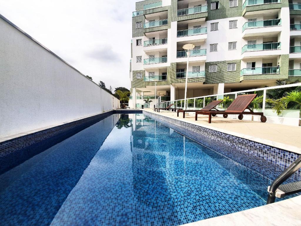 A well-maintained swimming pool is shown, featuring clear blue water that reflects the surrounding architecture. Sun loungers are positioned nearby, offering a relaxing spot for enjoyment. The modern condominium building is visible in the background, surrounded by greenery.