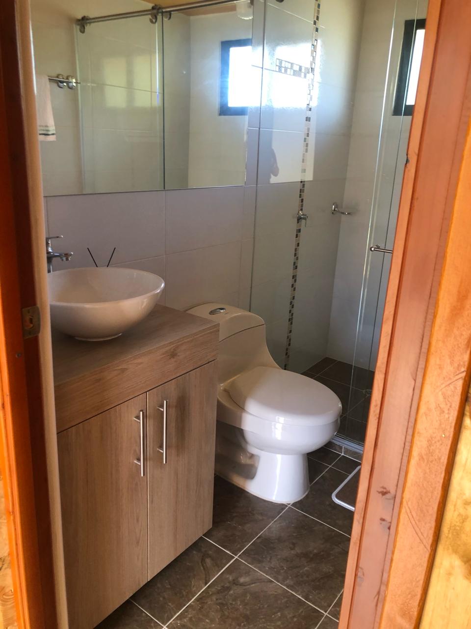 The bathroom features sleek tile walls and modern fixtures. A spacious vanity is equipped with a bowl sink, while a glass-enclosed shower is present. Light enters through a window, creating a bright, airy environment. Neutral tones promote a calming atmosphere.