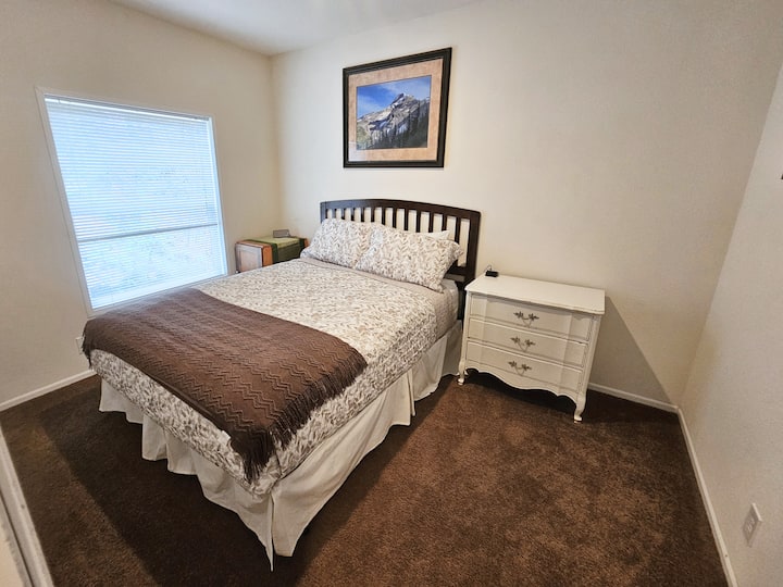 غرفة نوم مريحة ذات طابع بني مع سرير بحجم كوين مريح. استخدم مكتبين صغيرين وخزانة مع شماعات لمتعلقاتك الشخصية.