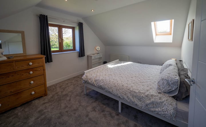 Veľká spálňa na poschodí s veľkou posteľou a otvoreným výhľadom na krajinu.