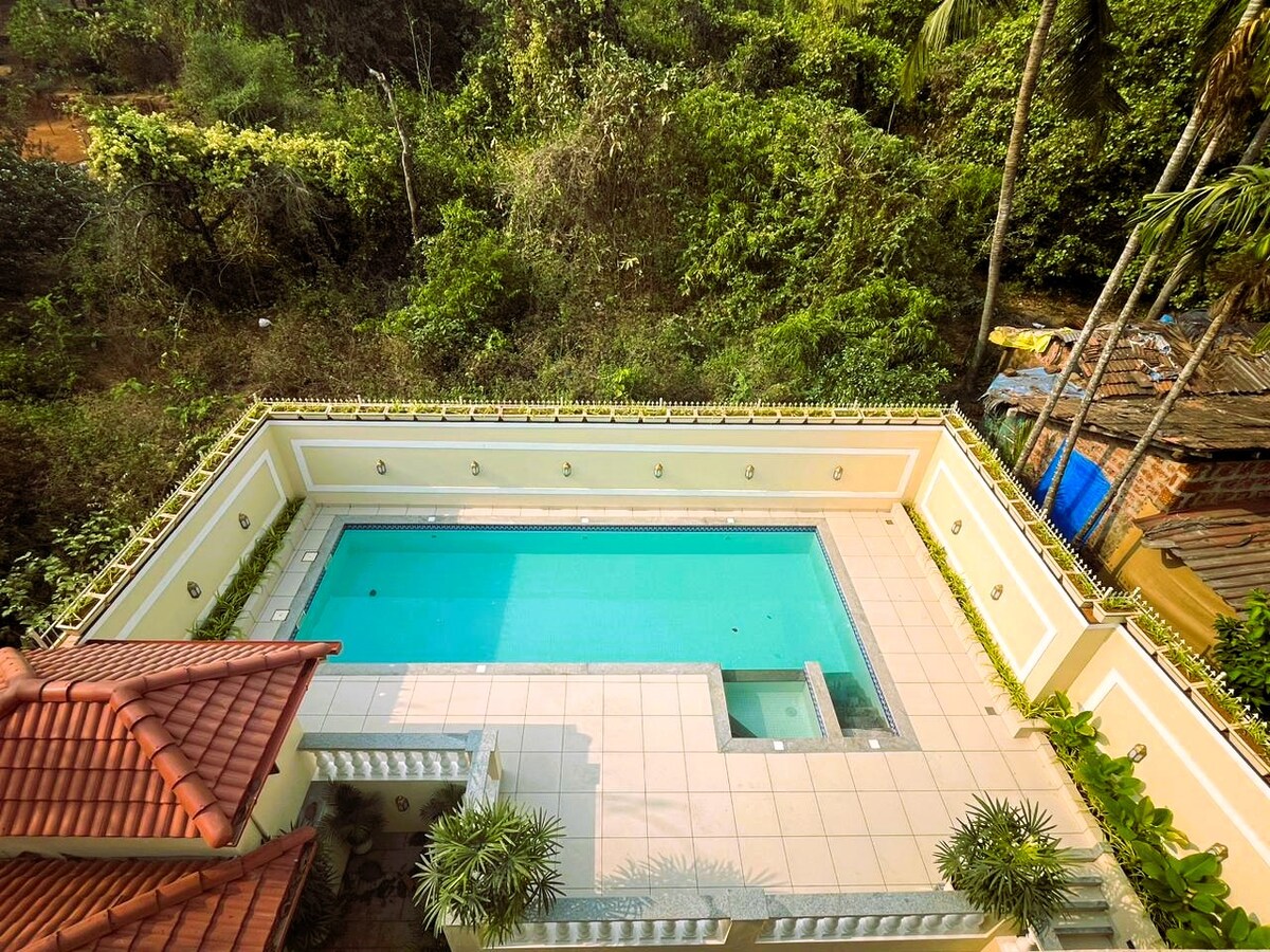 An outdoor swimming pool is surrounded by a well-maintained terrace, featuring clean lines and a smooth surface. Lush greenery and trees form a natural backdrop, providing privacy to the space. The pool is designed for relaxation and enjoyment, complementing the tranquil setting.