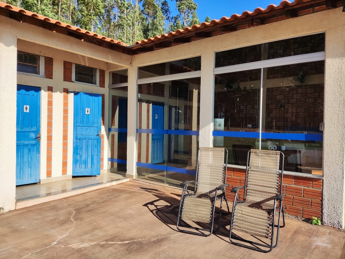 A patio area is visible, featuring two outdoor chairs arranged for relaxation. The entrance is framed by blue doors, and large glass windows provide a view into the communal space, allowing natural light to fill the interior.