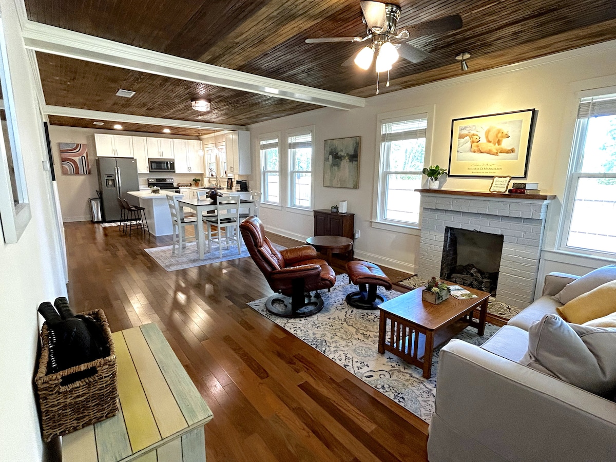 The living area features Brazilian Walnut hardwood floors and a tongue-and-groove ceiling. A natural gas fireplace is set between two windows. A pair of recliners and a coffee table is arranged around the area rug, while a comfortable sofa complements the space.
