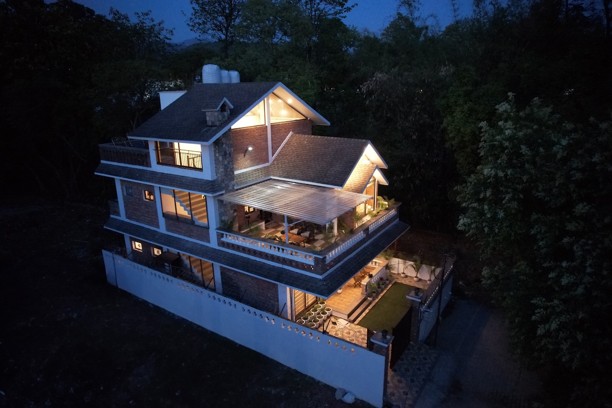 The three-story duplex villa is illuminated at night, showcasing its inviting architecture. Large windows allow for a blend of indoor and outdoor living, while the terrace is highlighted as an area for relaxation. Surrounding greenery enhances the tranquil setting of the property.