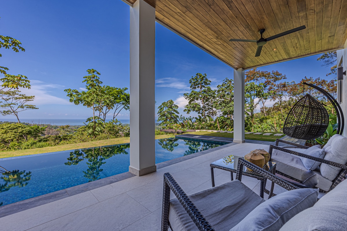 An inviting outdoor space features a private pool, surrounded by lush greenery and stunning ocean views. Comfortable seating with soft cushions offers a relaxing spot to enjoy the tranquil atmosphere under a spacious ceiling, complemented by a sleek ceiling fan.