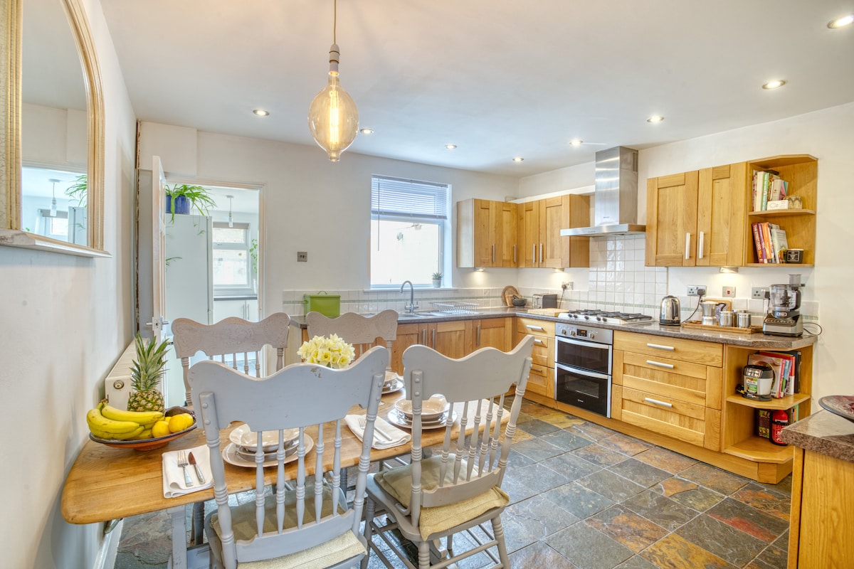 A large kitchen is highlighted by wooden cabinetry and a spacious dining table with seating for six. Modern appliances complement the cooking area, while natural light floods in through the windows, creating an inviting environment for meal preparation and dining.