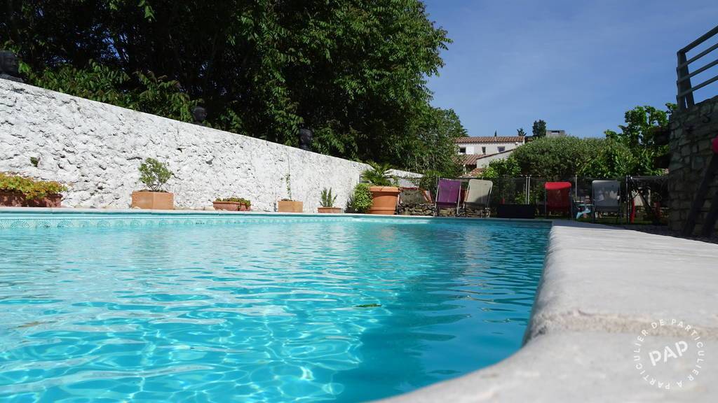 A tranquil swimming pool reflects the blue sky, surrounded by green trees and neatly arranged potted plants. The pool area is lined with lounge chairs, creating a serene outdoor relaxation space. A low stone wall borders the pool, enhancing the peaceful atmosphere.