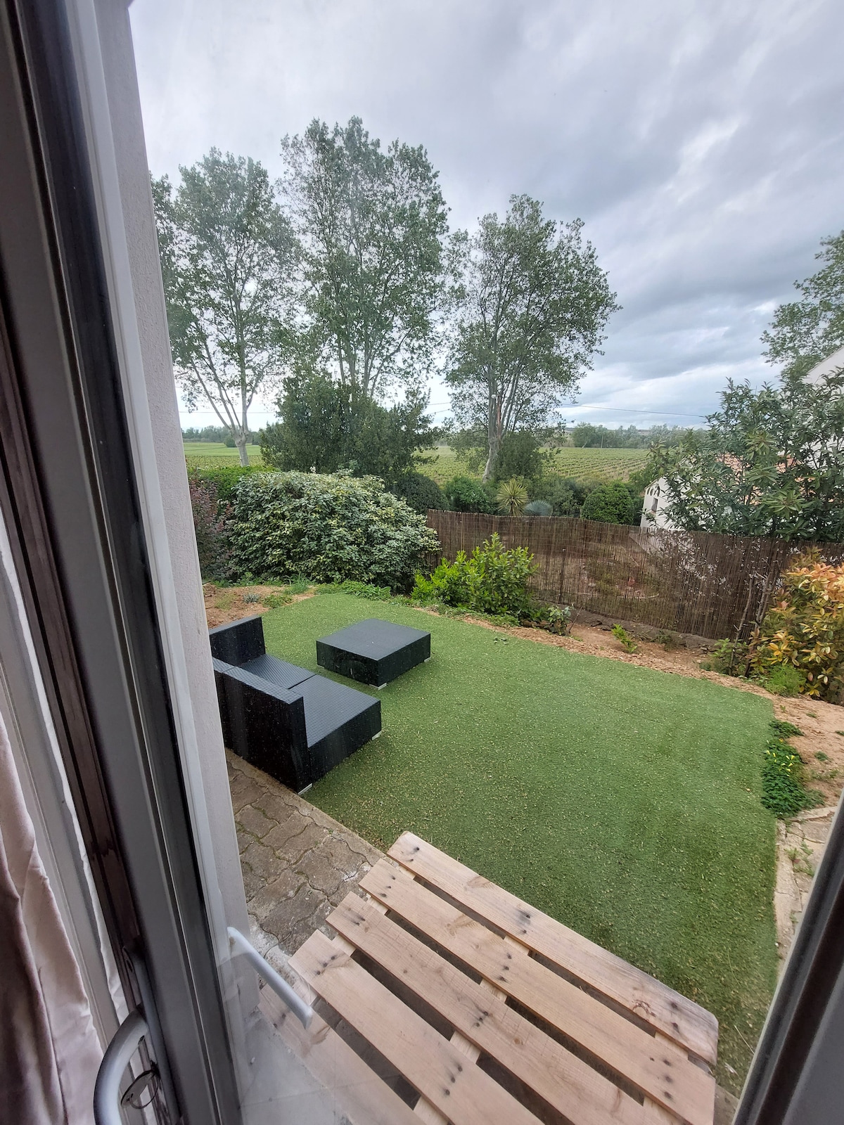 A private terrace is visible, featuring a small grassy area adorned with two dark seating arrangements. Surrounding greenery and trees provide a natural backdrop, with an open view of the distant landscape. A portion of the patio is shown, enhancing the outdoor space.