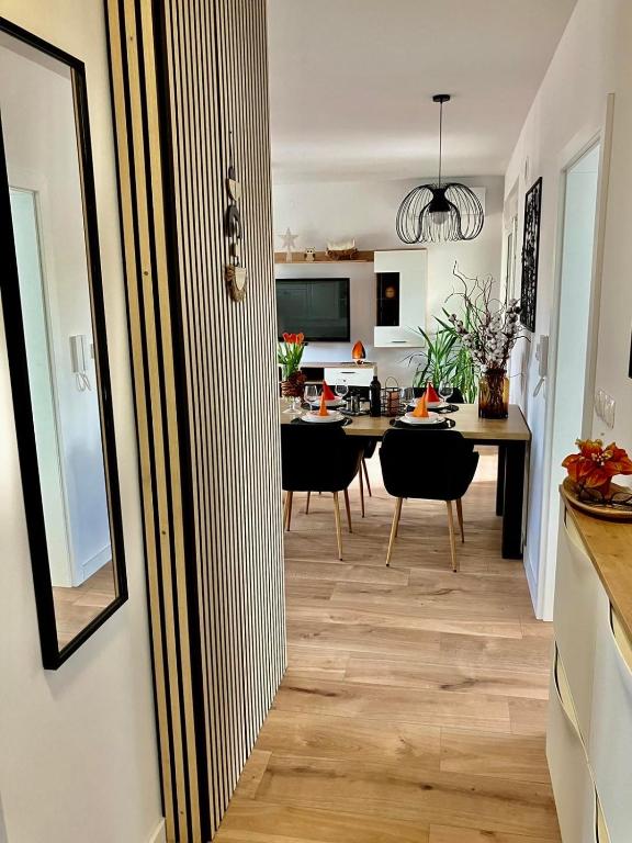 A hallway leads to a dining area featuring a dark wooden table set for a meal with elegant tableware. Black chairs provide seating, and a stylish pendant light hangs above. The space is accented by decorative plants and wooden flooring that enhances the modern design.