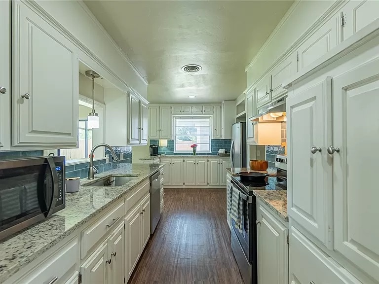 A well-equipped kitchen features light-colored cabinetry and a spacious layout. Granite countertops provide ample preparation space, while modern appliances, including an oven and microwave, are clearly visible. A window allows natural light, illuminating a central area with decorative accents, enhancing the inviting environment.