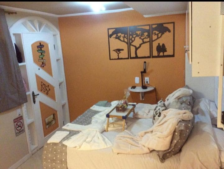 The room features an orange accent wall with decorative wall art depicting trees and silhouettes of birds. A spacious bed is adorned with soft blankets, while a small table with a decorative item is positioned beside it. A door adds character to the space.