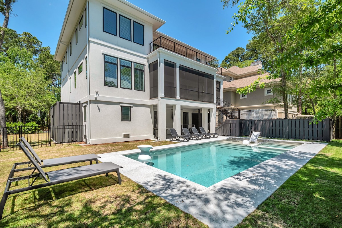 The outdoor area features a private swimming pool surrounded by a sun shelf and a spacious patio. Lounge chairs are positioned alongside the pool, with a shaded area provided by the home's overhang. The backyard is enclosed by a fenced landscape, offering privacy.