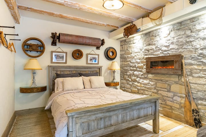 A queen size farm house bed with a comfortable memory foam mattress  sits amongst natural sisal rugs, original mill artifacts and the stone wall with an electric fireplace.  A window, opposite opens to listen to the river outside.