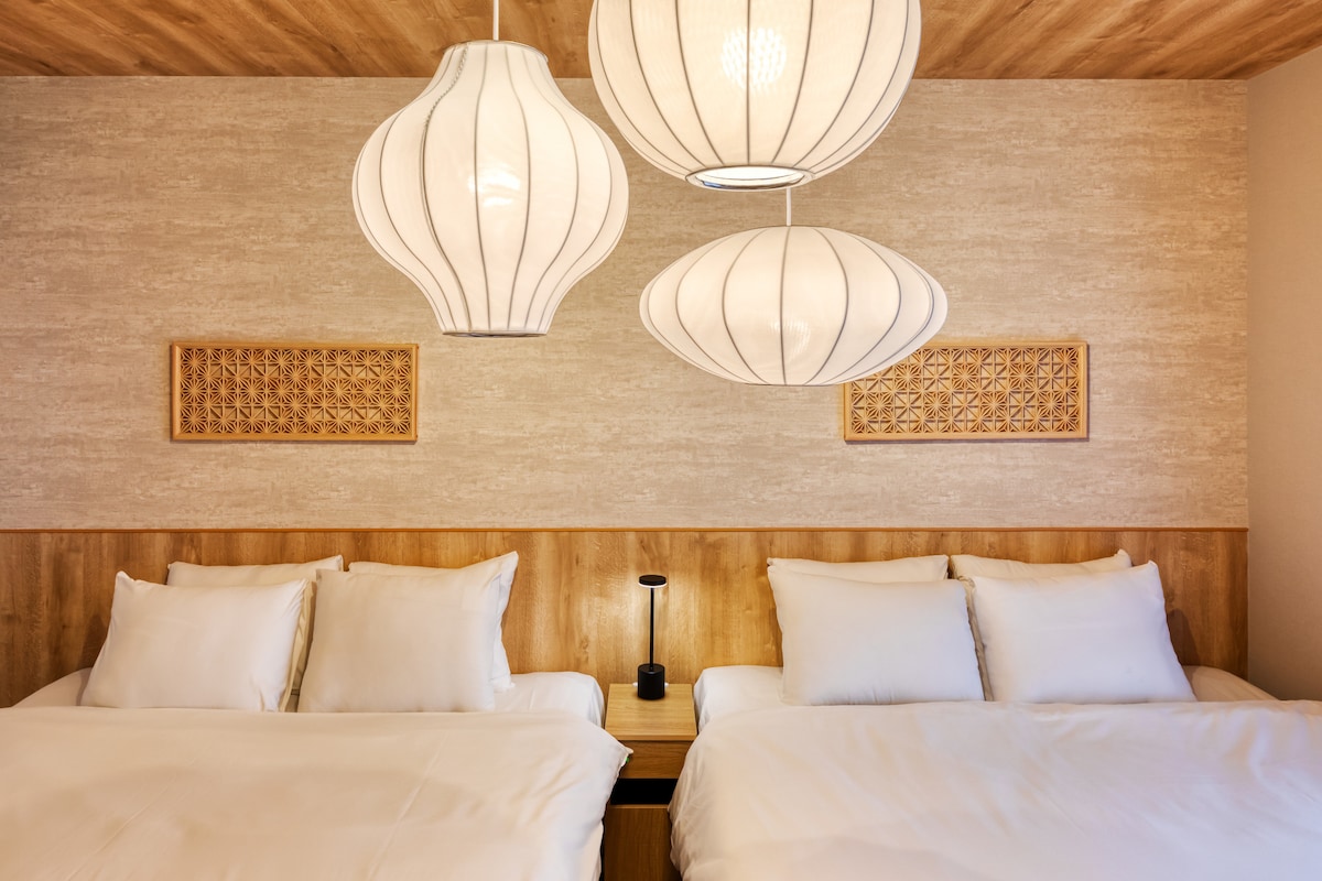 A comfortable sleeping area features two spacious beds with neatly arranged white bedding. Above, three pendant lamps provide soft lighting, while decorative wood panels adorn the wall, adding a touch of warmth to the room.