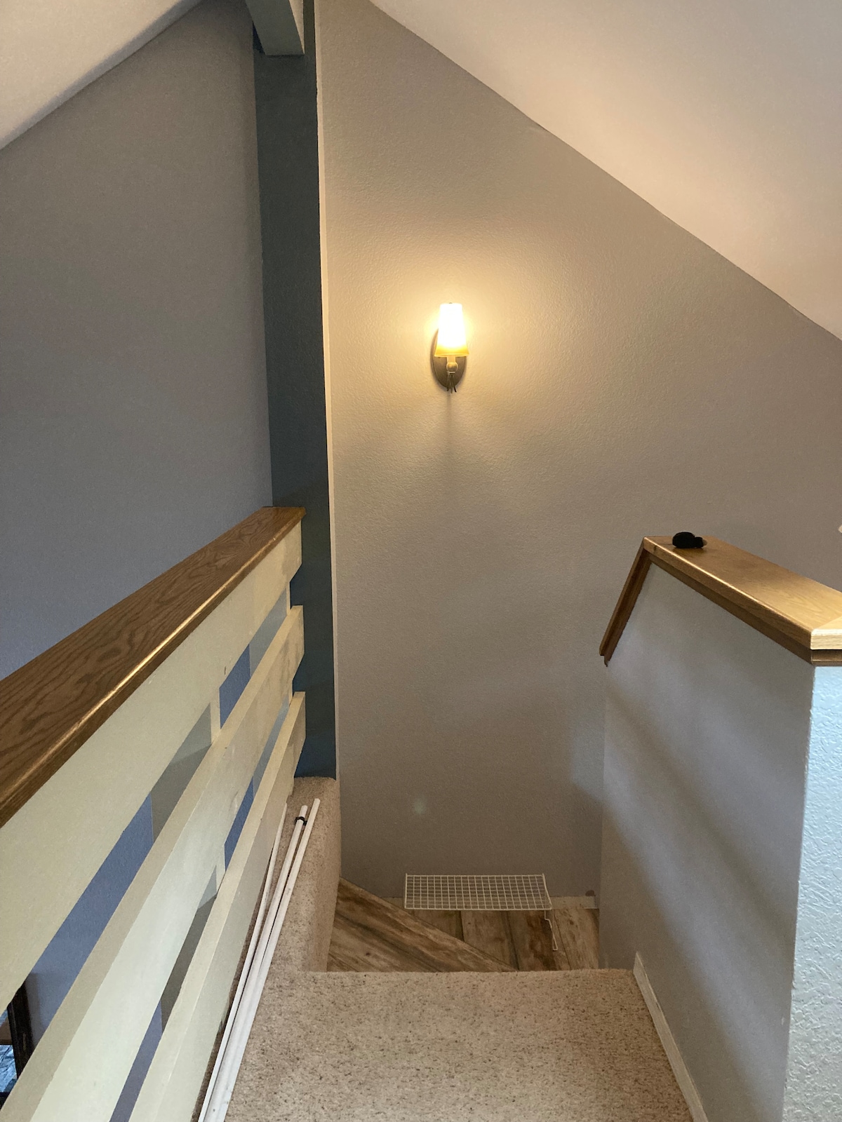 The staircase leads upward, framed by a wooden railing. A wall sconce provides soft lighting along the wall, enhancing the neutral-colored decor. The carpeted steps and smooth, painted walls create a clean and inviting atmosphere.