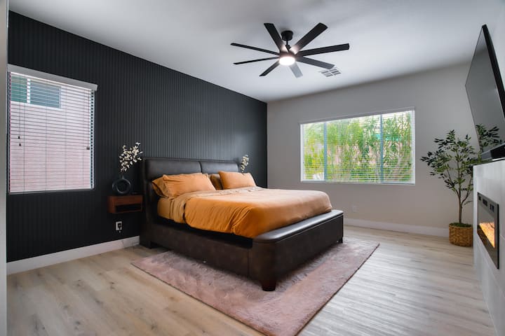 Ukuta mzuri wa rangi nyeusi huunda mandharinyuma ya kitanda cha ukubwa wa kifalme, kilichopambwa kwa mashuka laini ya machungwa kwa ajili ya joto