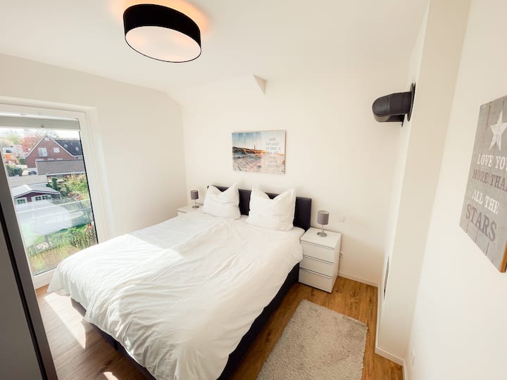 Manželská posteľ so svetlou posteľnou bielizňou a výhľadom z okna