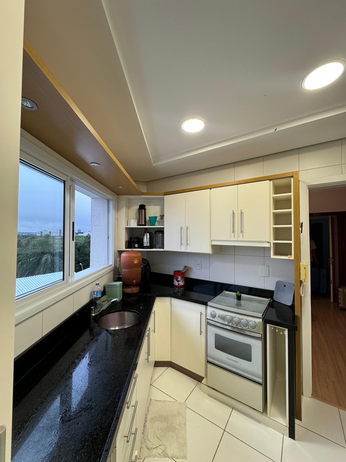 A well-equipped kitchen features a black granite countertop and white cabinet doors. Various appliances, including a stove and a coffee maker, are arranged for convenience. A large window allows natural light to fill the space, offering a view of the outdoors.