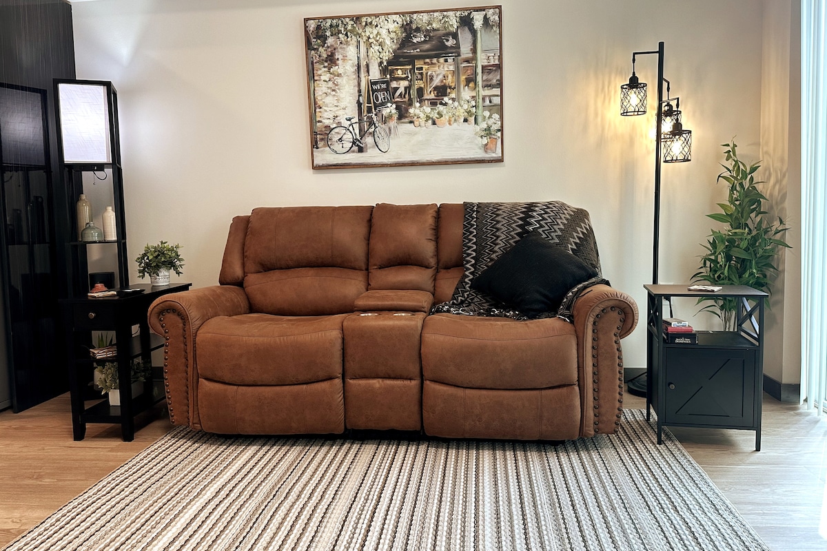 Living Room Space with brand new comfy couch that reclines on both ends and the center has a storage area and table cup holders.
