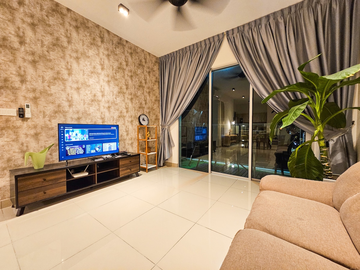 A living area features a spacious sofa, a sleek entertainment unit with a Smart TV, and large glass doors that lead to an outdoor space. Soft curtains frame the windows, and a green plant adds a touch of nature to the room.