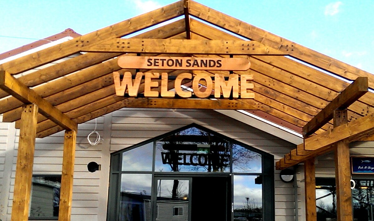 A wooden entrance structure features a sloped roof and prominently displays the word 'WELCOME' at its center. Large glass doors provide visibility into the reception area, framed by white walls, creating an inviting first impression for guests.