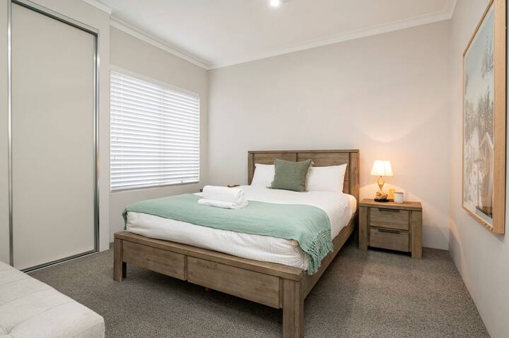 Accogliente camera da letto con un comodo letto matrimoniale, lenzuola morbide e un'elegante coperta verde. Dispone di comodini con lampade per la lettura, ampia luce naturale attraverso tapparelle e armadio a muro.