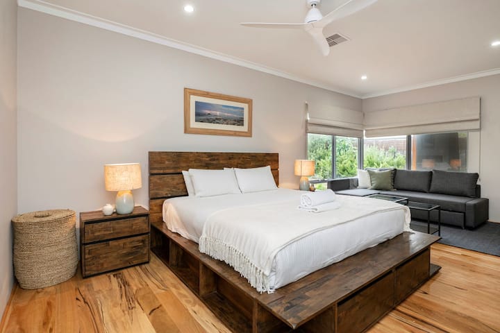 Elegante camera da letto con letto matrimoniale grande con struttura in legno, comode lampade da comodino e ventilatore sul soffitto. Include un'ampia area salotto con divano, perfetta per rilassarsi, e ampie finestre per la luce naturale.