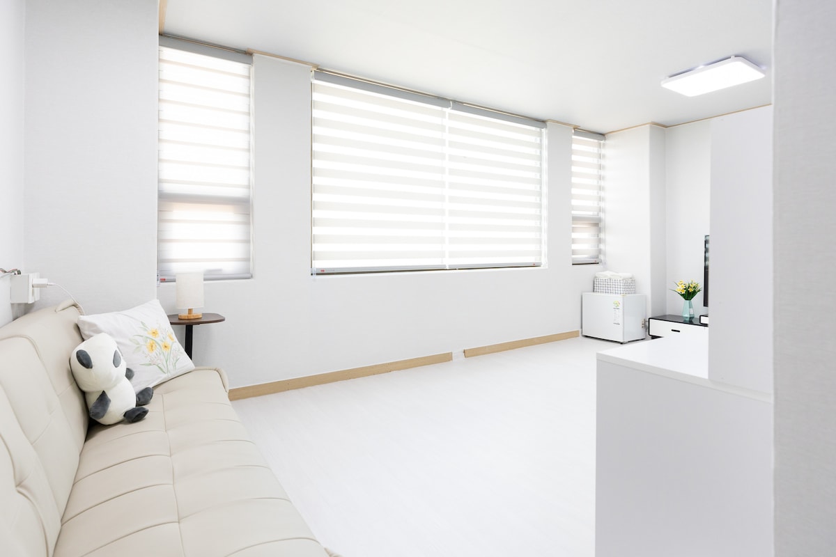A bright and airy living space features large, horizontally striped windows that allow natural light to fill the room. A light-colored sofa is positioned against the wall, complemented by a small side table. Minimalist decor creates a clean and open atmosphere.