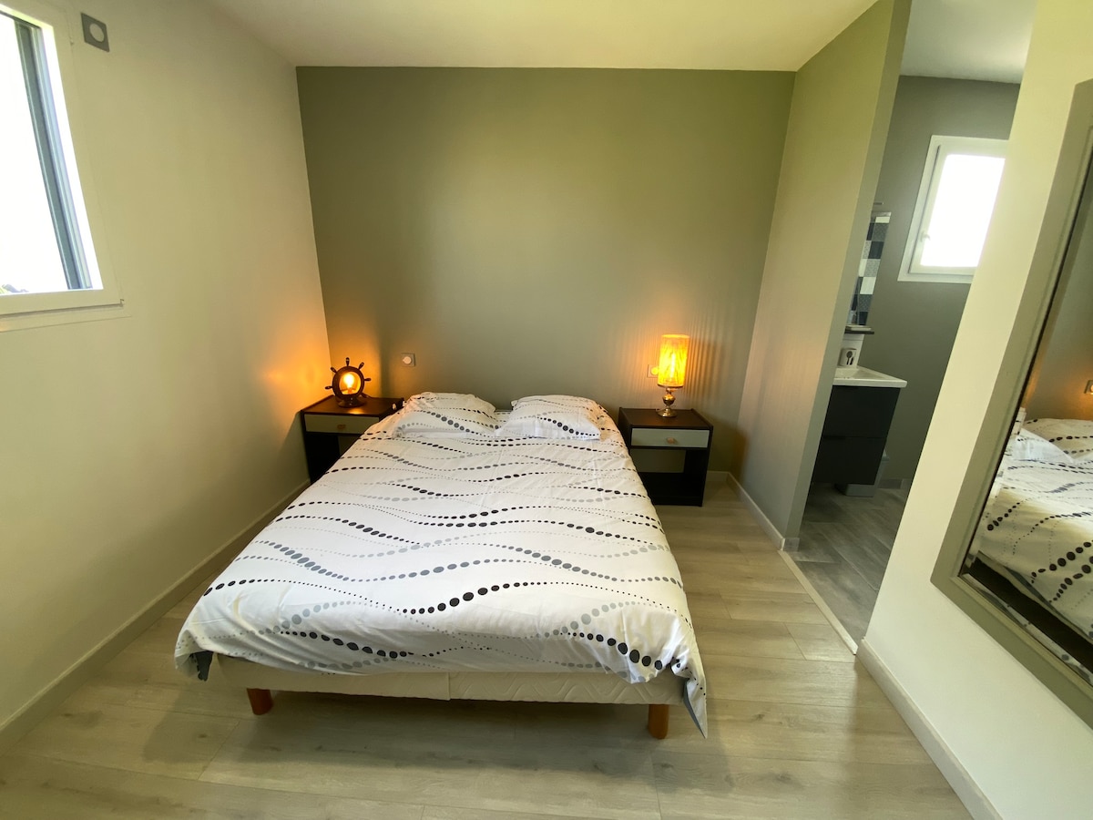 A well-lit bedroom features a spacious bed covered with a white duvet adorned with black polka dots. Nightstands are positioned on either side, each with a lamp that provides a warm glow. Light-colored walls reflect natural light from a window.