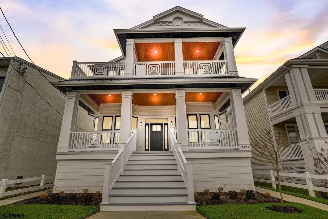 The exterior of the two-story condo showcases a classic architectural design with a large front staircase leading to a welcoming entrance. The porch is adorned with railings and features overhead lighting, while well-maintained landscaping complements the white siding and modern details.